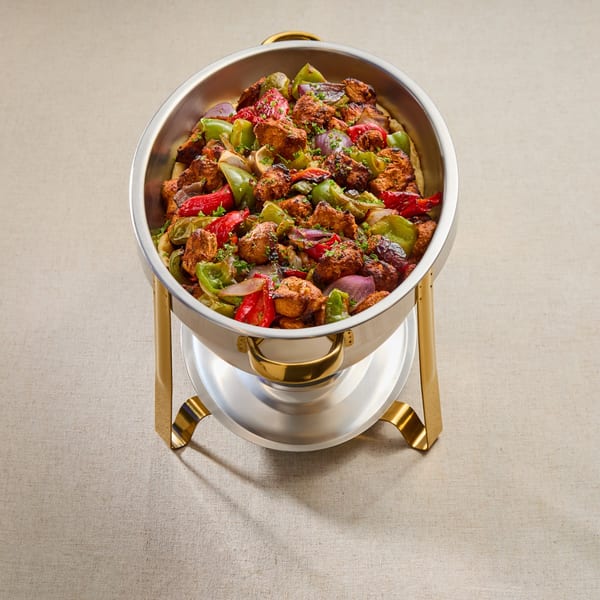 A large silver chafing dish filled with Mediterranean chicken, red and green bell peppers, and onions.