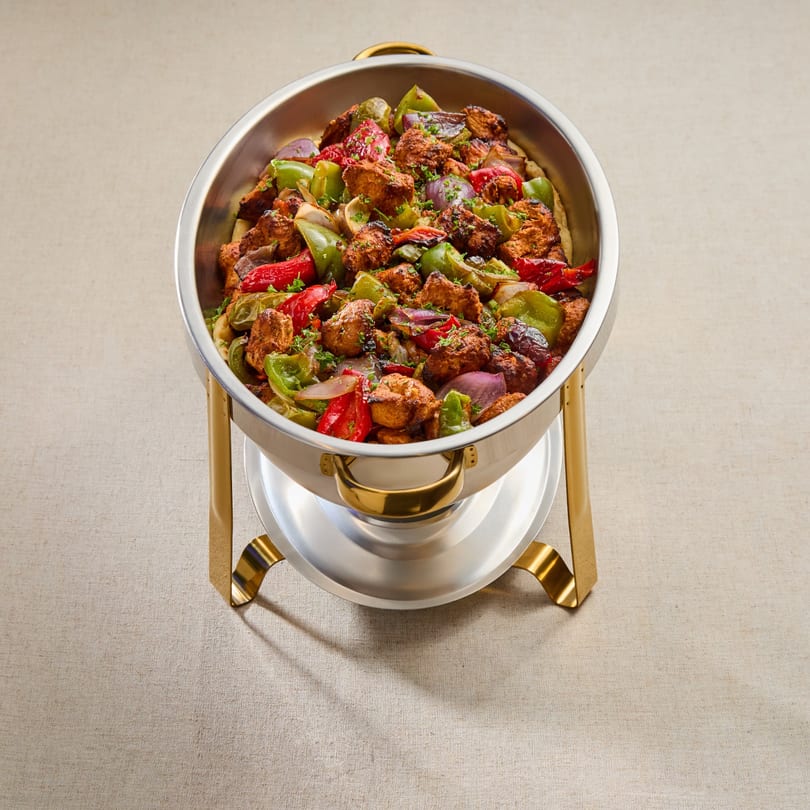 A large silver chafing dish filled with Mediterranean chicken, red and green bell peppers, and onions.