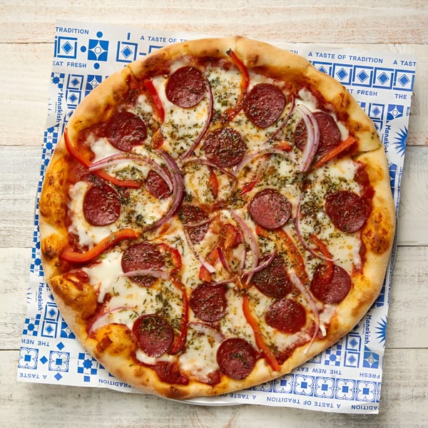 A pepperoni pizza with red onions and bell peppers on a blue and white patterned paper.