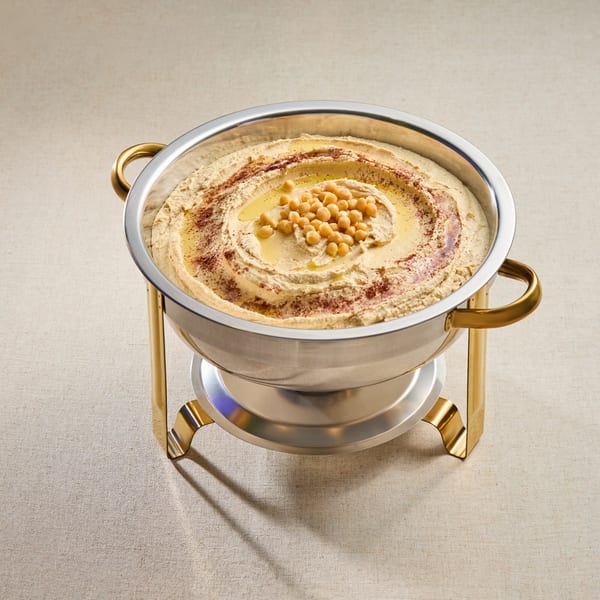 Creamy hummus in a silver bowl with gold handles, topped with chickpeas, olive oil, and paprika.