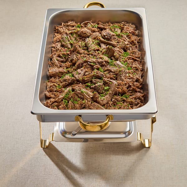 Shredded beef or lamb, garnished with parsley, in a stainless steel chafing dish.