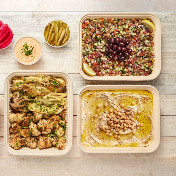 Mediterranean spread with hummus, salad, roasted vegetables, pickles, and sauce on a wooden table.
