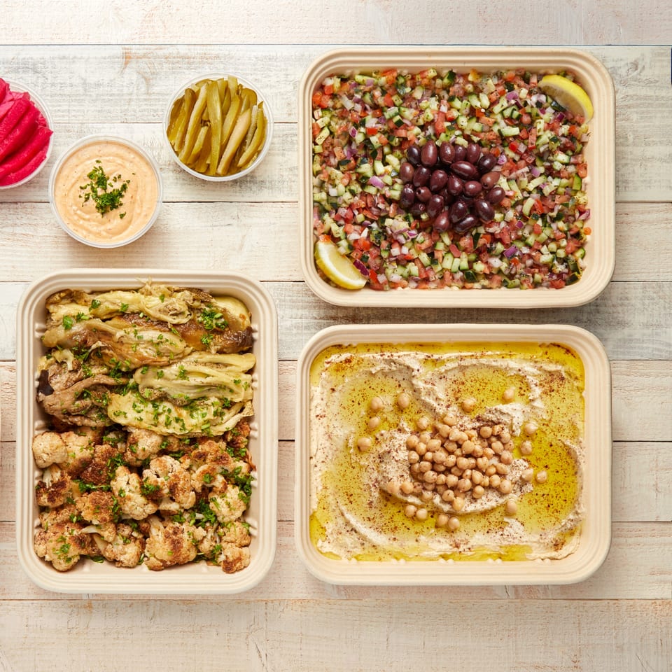 Mediterranean spread with hummus, salad, roasted vegetables, pickles, and sauce on a wooden table.