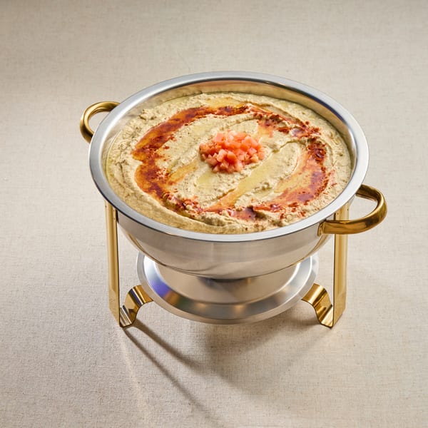 A large silver bowl of creamy hummus, drizzled with olive oil, paprika, and diced tomatoes.