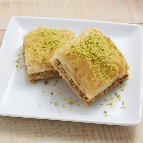 Two pieces of baklava, topped with crushed pistachios, on a white rectangular plate.