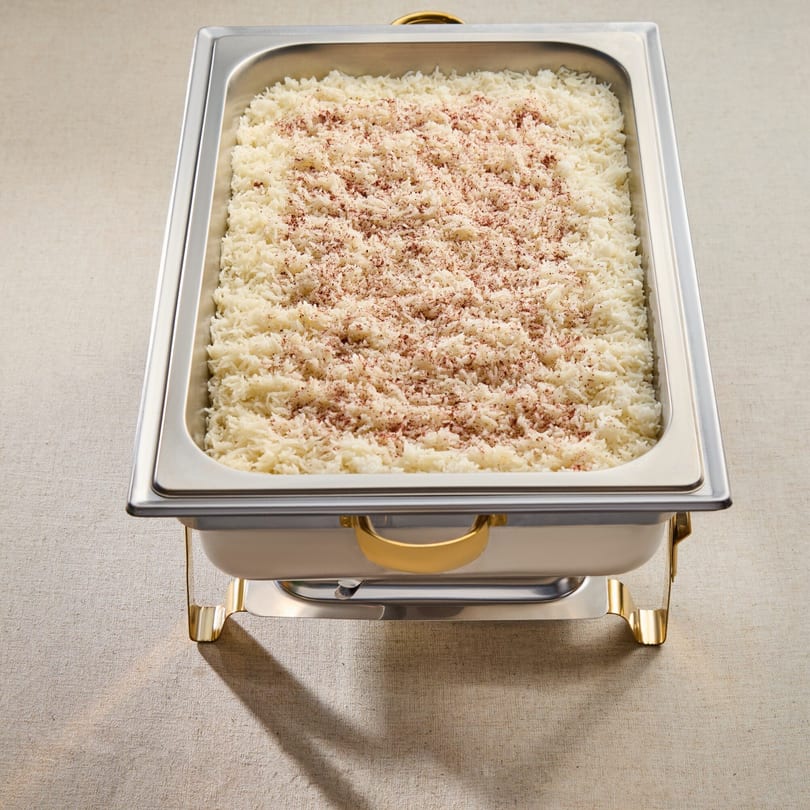 A large catering pan filled with white rice, lightly sprinkled with a reddish-brown spice.