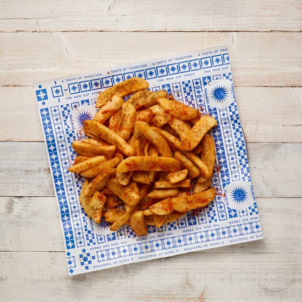 Seasoned potato wedges on a blue and white patterned paper from Manakish Oven & Grill.