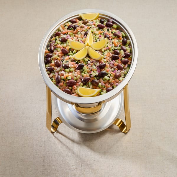 Chopped Mediterranean salad with olives and lemon wedges in a silver and gold serving dish.
