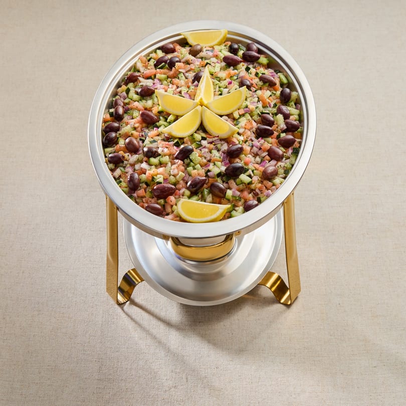 Chopped Mediterranean salad with olives and lemon wedges in a silver and gold serving dish.